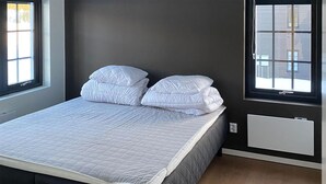 A neatly made bed with a quilted white duvet and pillows, positioned in a room with a dark wall and a window. - Stunning apartment in Idre with sauna (Idre)
