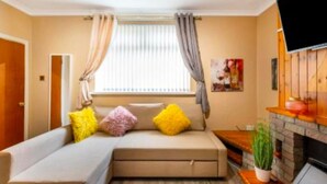 Ein gemütliches Wohnzimmer mit einer Couch, Kissen, einem Kamin und einem Fernseher.