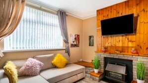 Ein Wohnzimmer mit einer Couch, einem Kamin und einem an einer Holzwand montierten Fernseher.