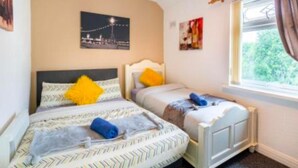Ein Hotelzimmer mit zwei Betten, einem Fenster mit Vorhängen und einem Stadtbild an der Wand.