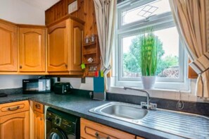 Une cuisine avec des meubles de rangement en bois, un évier et une fenêtre avec des rideaux.