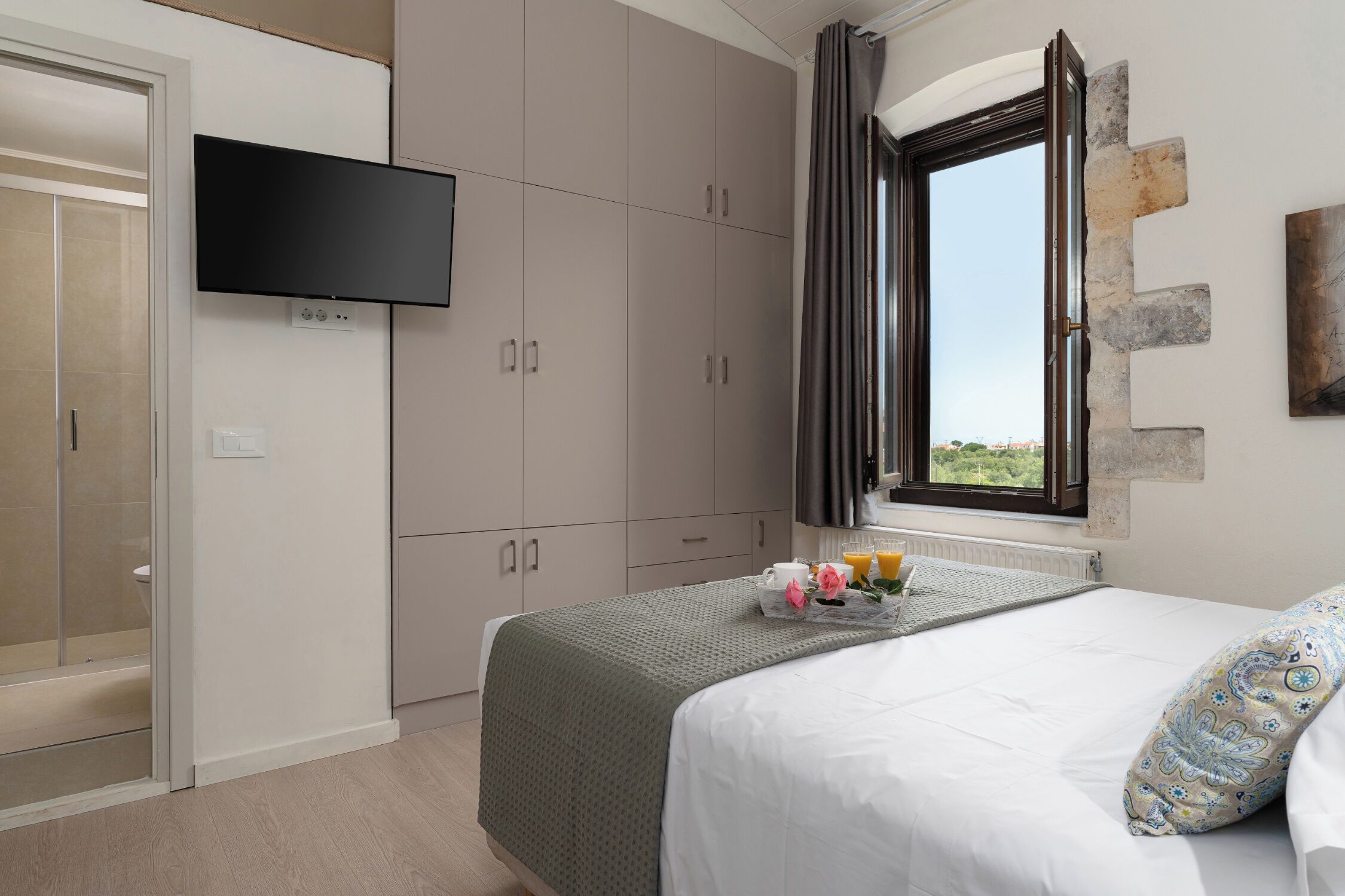 A bedroom with a bed, a TV mounted on the wall, and a window with curtains.