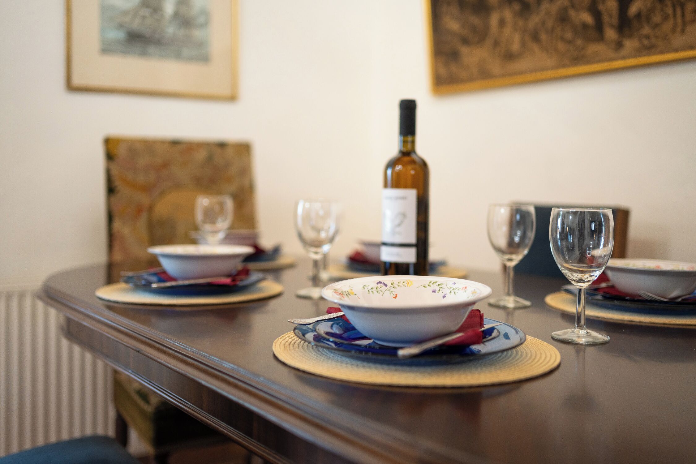 A dining table set with plates, bowls, and wine glasses, with a bottle of wine in the center.