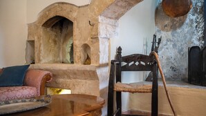 A room with a stone fireplace, a wooden chair, a sofa, and a wooden table. - The Olive Mill House Luxe Villa (Rethymno)