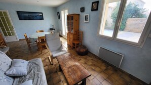 Een woonkamer met een bank, een houten tafel, stoelen en een kast. Er is een raam met uitzicht op het omliggende landschap.