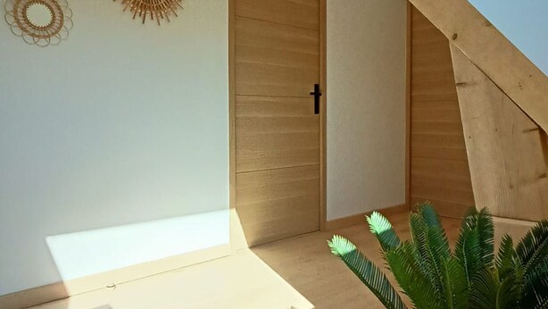 A room with a wooden door, a sunburst wall decoration, and a sloped ceiling.