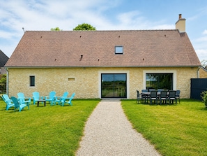 A stone building with a tiled roof, a gravel path, and outdoor seating with chairs.