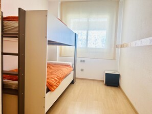 A bunk bed room with a window, a small heater, and a wall-mounted shelf. - Family Apartment with Garden, Pool, and AC near La Rubina Beach (Roses)
