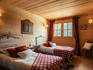 A cozy cabin-style room with two beds, a wooden ceiling, a window with curtains, and a small table with a lamp. - 4★ Chalet, 5 beds, outdoor spa, near shuttle, pets welcome (La Clusaz)