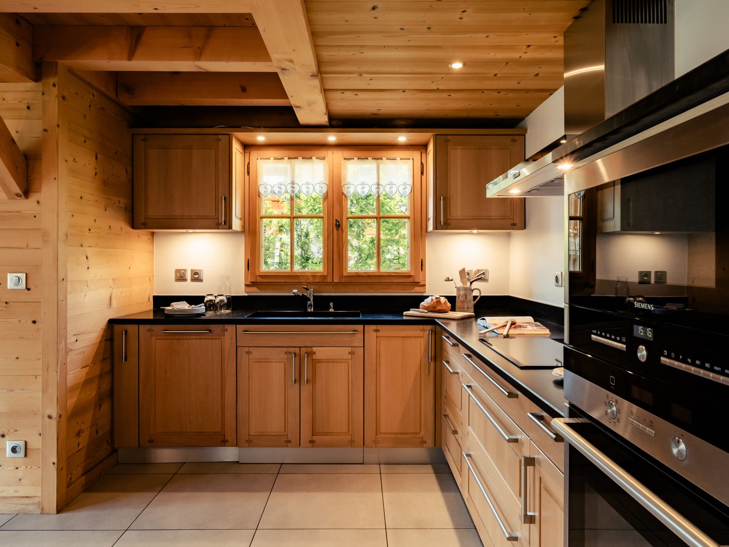Una cocina moderna con armarios de madera, encimera negra y electrodomésticos de acero inoxidable.