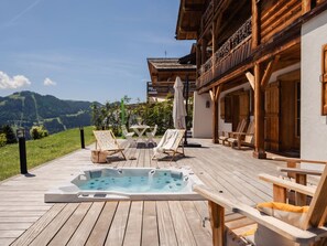 A wooden deck with a hot tub, lounge chairs, and a table with umbrellas.