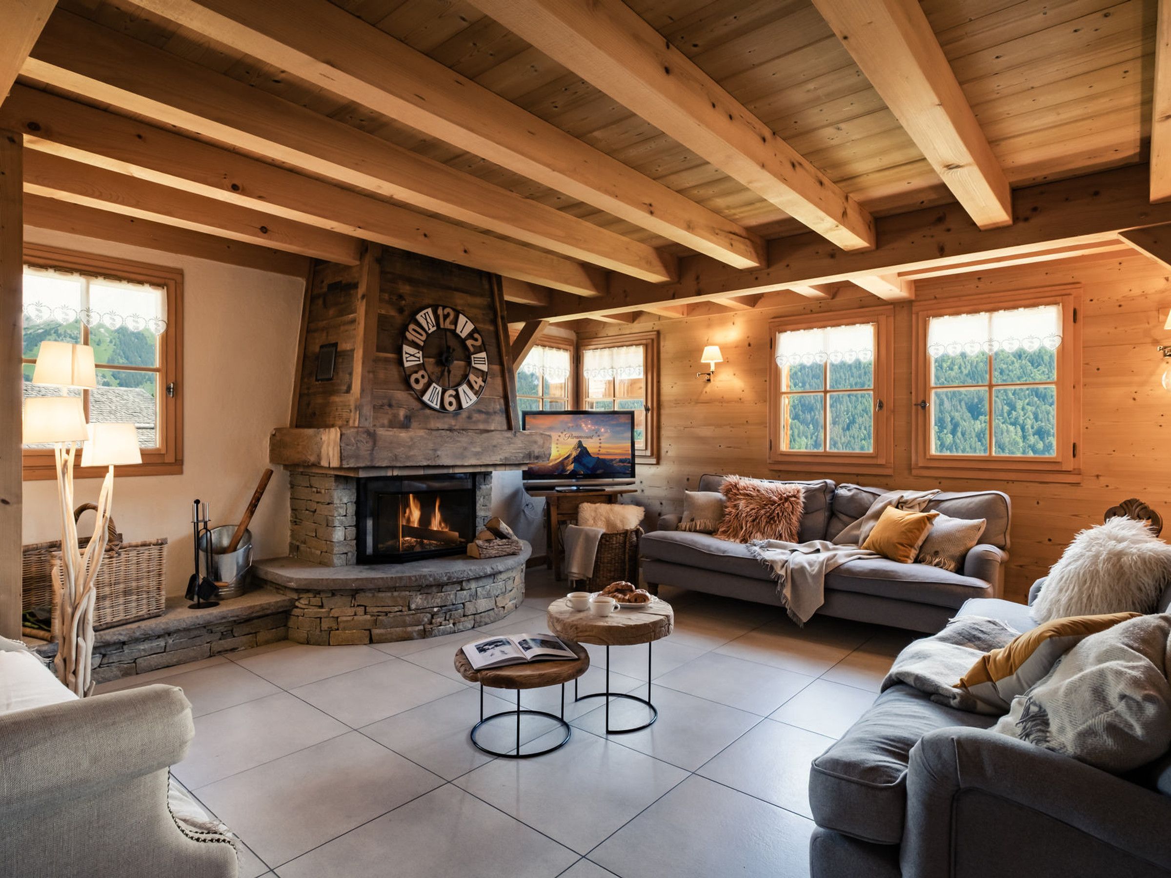 Ein gemütliches Wohnzimmer mit Kamin aus Stein, Holzbalken, einer Couch und einem Fernseher.