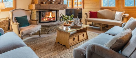 Una sala de estar acogedora con chimenea de piedra, vigas de madera y ventanas amplias que ofrecen vistas al exterior.