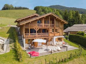 Un chalet de madera con balcón, mobiliario exterior y vistas a un paisaje montañoso.