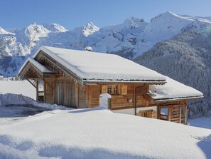 A wooden cabin with a snow-covered roof, set against a backdrop of snow-covered mountains. - 4★ Chalet, 5 beds, outdoor spa, near shuttle, pets welcome (La Clusaz)