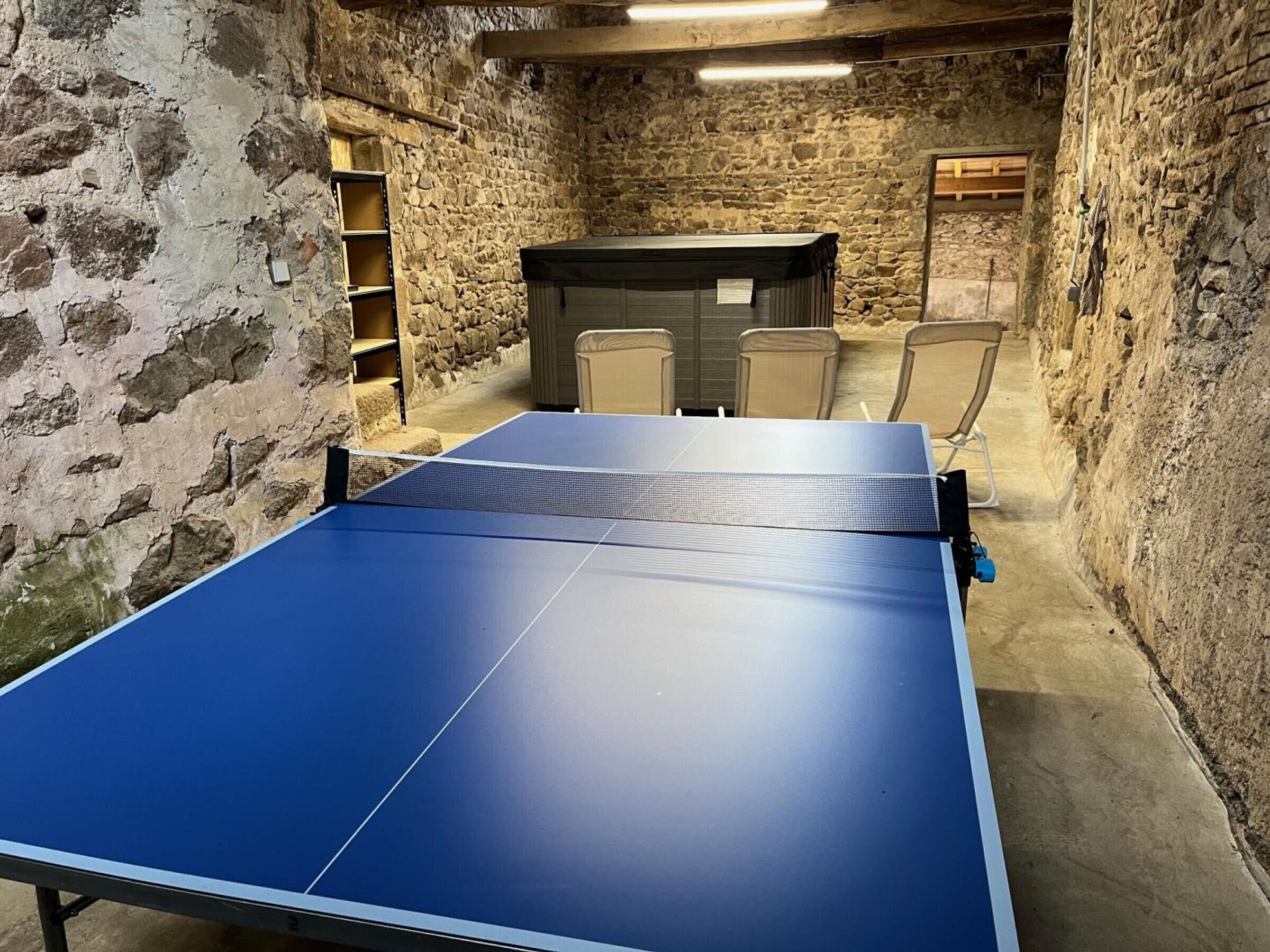 Une table de ping-pong dans une pièce aux murs de pierre, avec un banc et des étagères.