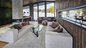 A modern living room with a glass coffee table, white sofas, and a large window offering a view of a snowy landscape.