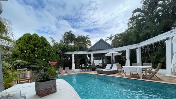 A pool area with lounge chairs, a covered seating area, and a table with a glass of water and a plate.