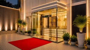 A hotel entrance with a red carpet, glass doors, and potted plants.