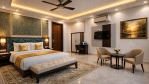 A modern hotel room with a large bed, a desk, two chairs, a ceiling fan, an air conditioning unit, and a painting on the wall. - Hotel Palm View by JMD Group (New Delhi)