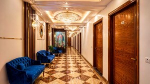 A hotel lobby with a checkered floor, blue sofas, chandeliers, and wooden doors. - Hotel Palm View by JMD Group (New Delhi)