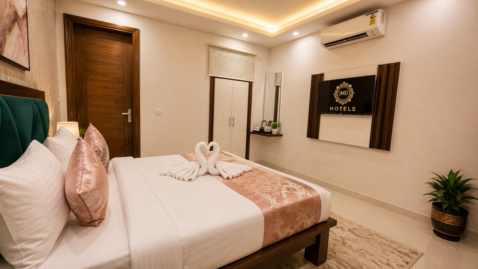 Une chambre d’hôtel avec un lit, une porte en bois, un miroir, un climatiseur fixé au mur et un panneau indiquant « JMD Hotels ».
