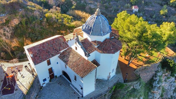 A white building with a dome and red-tiled roof, surrounded by trees and a stone wall. - Cau de l'Art (Llucena)