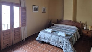 A bedroom with a bed, a nightstand, a window with curtains, and two framed pictures on the wall. - Cau de l'Art (Llucena)
