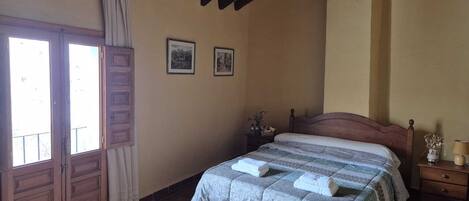 A bedroom with a bed, a nightstand, a window with curtains, and two framed pictures on the wall.