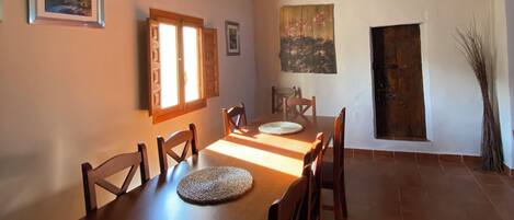 A dining area with a wooden table and chairs, a window with blinds, and a door.