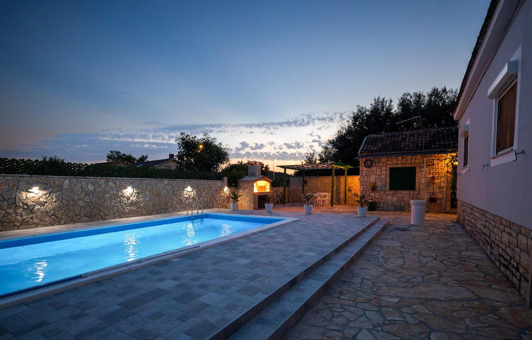 A swimming pool with stone walls and steps leading to a stone building with outdoor seating.