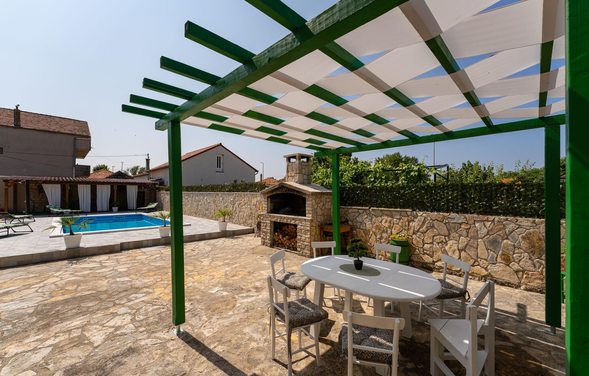 Zona exterior coberta amb una barbacoa de pedra, una piscina i una taula amb cadires.