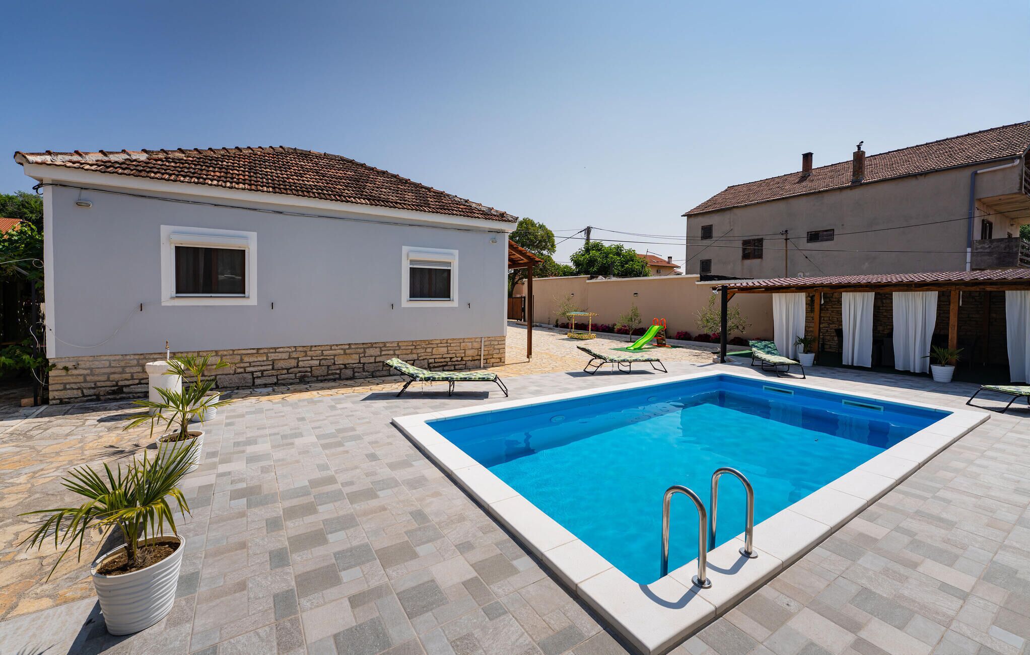 Ein rechteckiger Pool mit zwei Leitern, umgeben von einer gefliesten Terrasse.