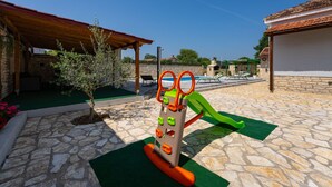 Un terrain de jeux équipé d’une balançoire et d’une structure d’escalade, entouré de murs en pierre et comprenant un espace piscine.