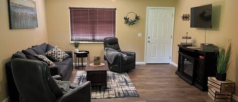 A living room with a sofa, two recliners, a coffee table, a fireplace, a television, and a ceiling fan.