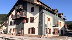 A two-story building with a balcony, a garage door, and a sign indicating a restaurant. - Apartment in the heart of the High Vosges! (Cornimont)