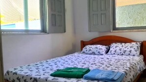 A single bed with a patterned bedspread, two pillows with a similar design, and a green and blue towel on the bed.