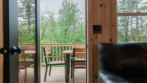 A wooden cabin interior with a black leather couch, a wooden deck with outdoor furniture, and a door leading outside. - The Mont Haus- WOOD FIRED SAUNA - Minutes to Mt. Snow and Stratton! (Wardsboro)