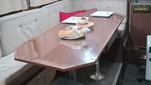 Een gezellig eetgedeelte met een tafel, een comfortabele bank, een klein krukje en een koelkast.