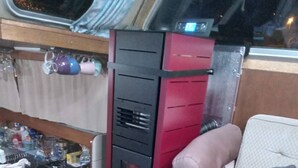 Een gezellig interieur met een bank, een kleine tafel met een bloevas, en een keukenhoek met een fornuis en kastjes.