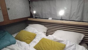 Een bed met witte beddengoed en twee kussens, één smaragdgroen en één geel, in een kamer met een houten hoofdbord en een gordijn.