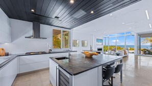 A modern kitchen with white cabinetry, a central island, and a large window offering a view of the outdoors.