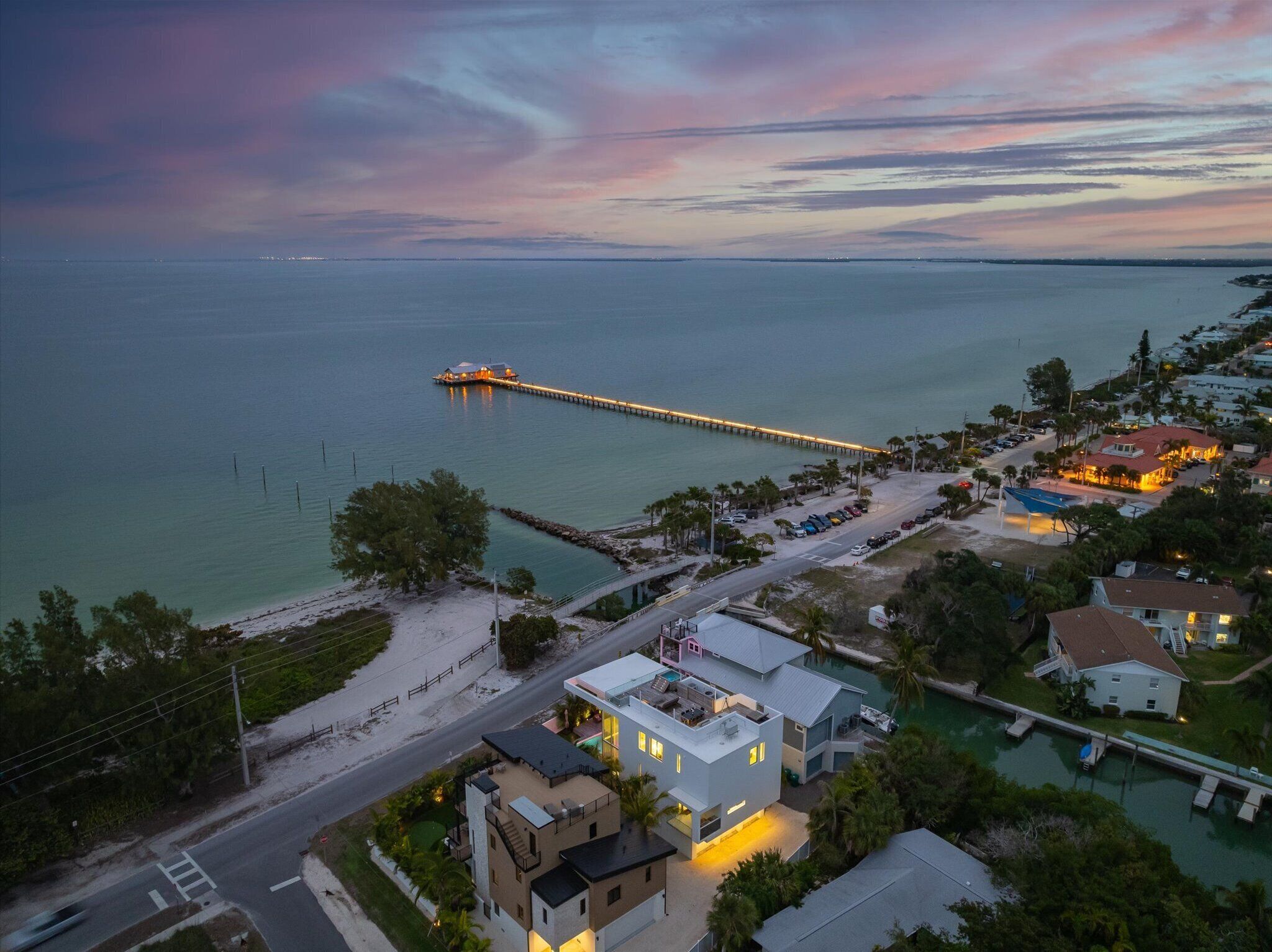 A coastal property with a dock extending into the water, a road leading to the property, and several buildings with visible balconies and outdoor areas.