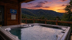 A hot tub with a wooden deck and a view of a sunset over a mountainous landscape. - 5BR w/MTN Views*Firepit*Hot Tub*Theater*Games (Sevierville)