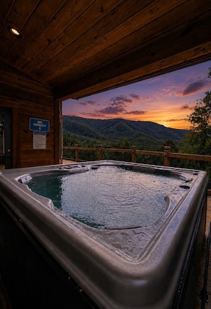 A hot tub with a wooden deck and a view of a sunset over a mountainous landscape.