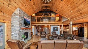 A spacious living room with a stone fireplace, leather sofas, and a high ceiling with exposed beams. - 5BR w/MTN Views*Firepit*Hot Tub*Theater*Games (Sevierville)