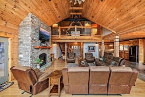 A spacious living room with a stone fireplace, leather sofas, and a high ceiling with exposed beams.