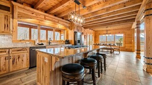 A spacious kitchen with wooden cabinetry, a large island with stools, and a view through the windows. - 5BR w/MTN Views*Firepit*Hot Tub*Theater*Games (Sevierville)