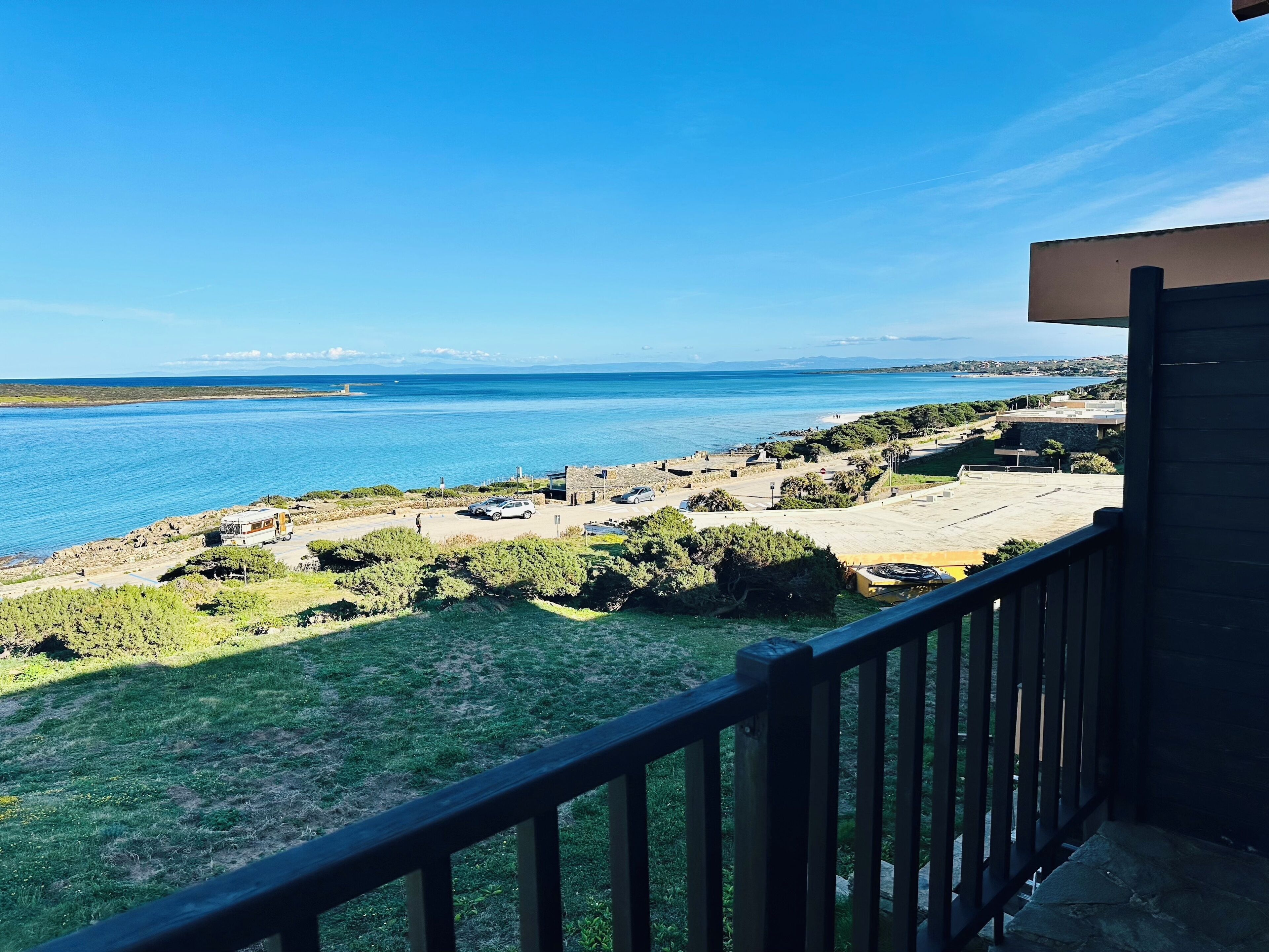 A coastal view from a balcony overlooking a beach area with a parking lot and buildings.