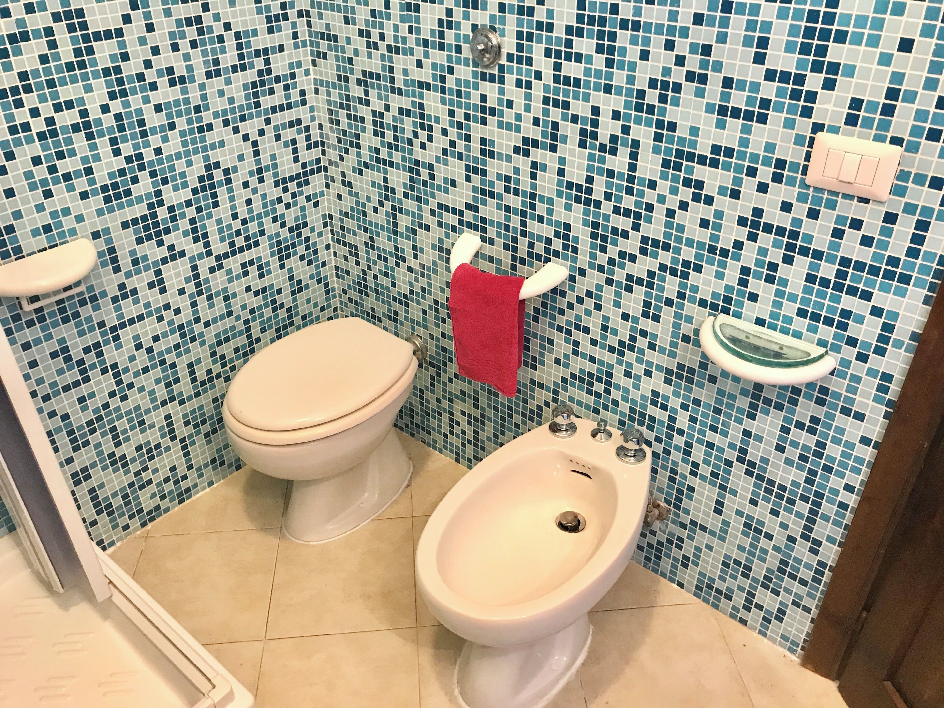 Un baño con inodoro, bidé y paredes de azulejos.